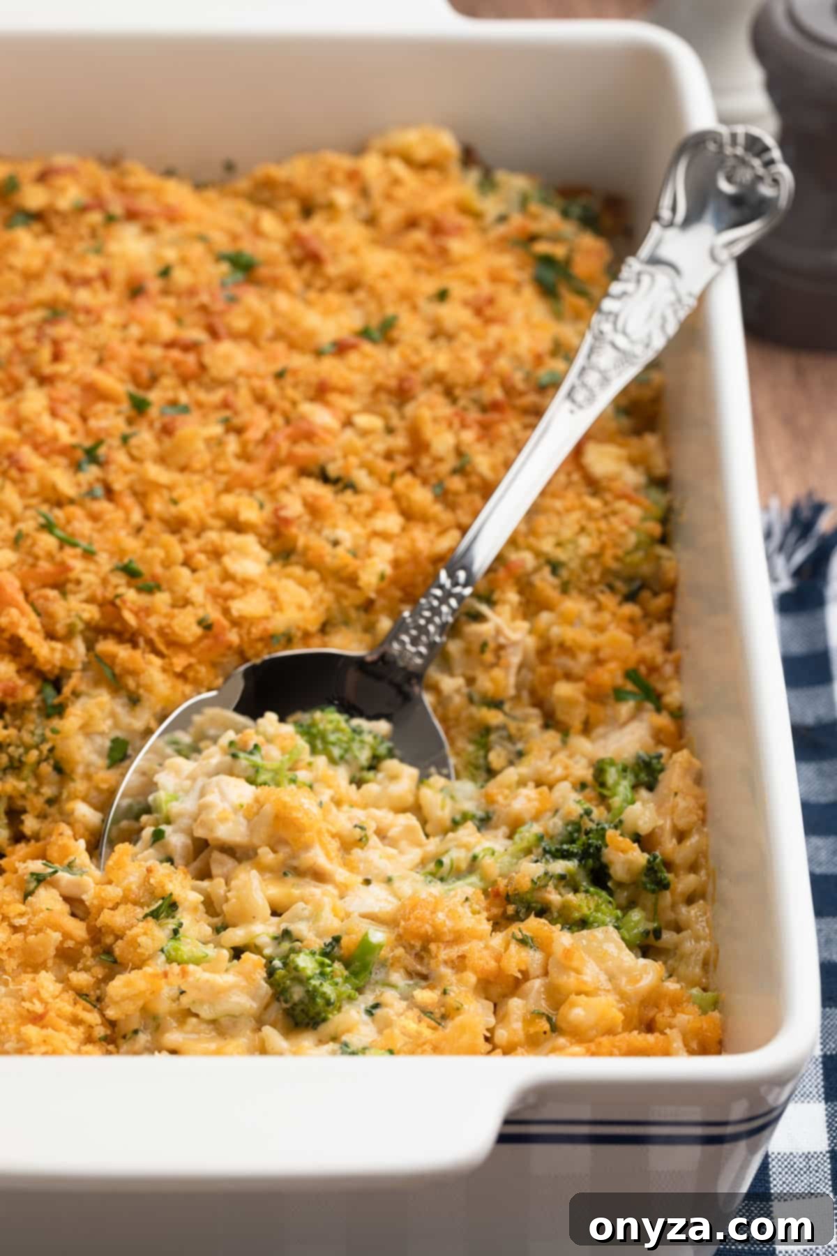 A comforting Chicken Broccoli Rice Casserole in a blue striped white baking dish, ready to be served with a silver spoon.