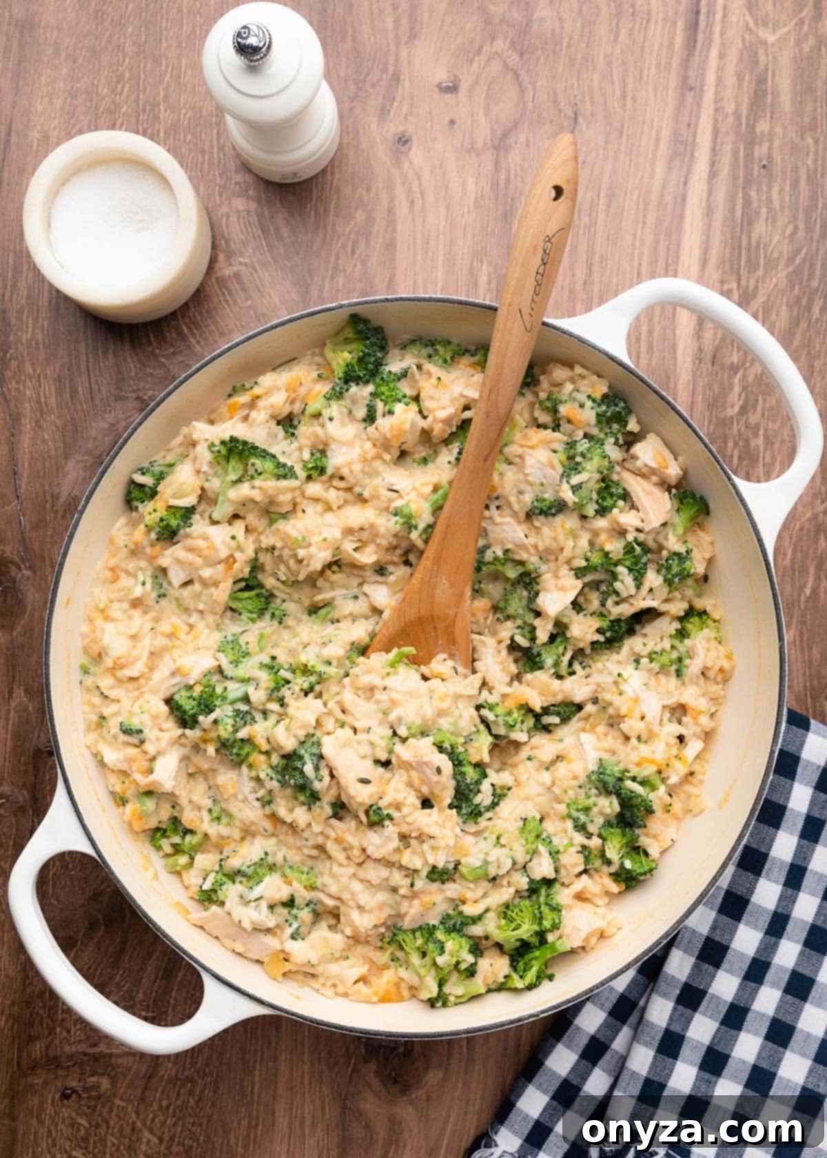 Unbaked chicken broccoli rice casserole mixture in a white enameled cast iron pot with a wooden spoon, perfectly mixed and ready for baking.