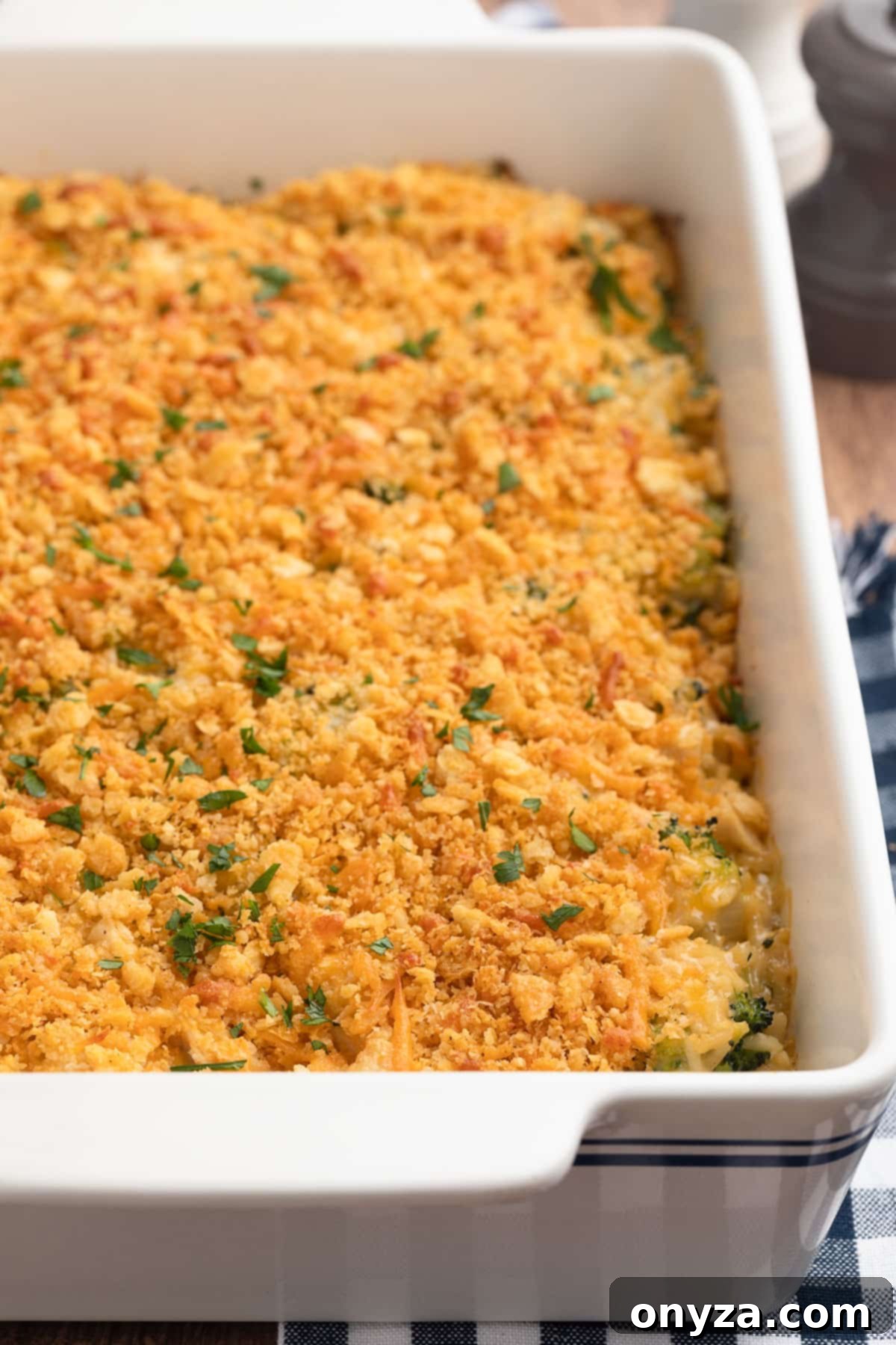 A freshly baked Chicken Broccoli Rice Casserole in a white baking dish, set on a blue and white checkered napkin, ready to be served.