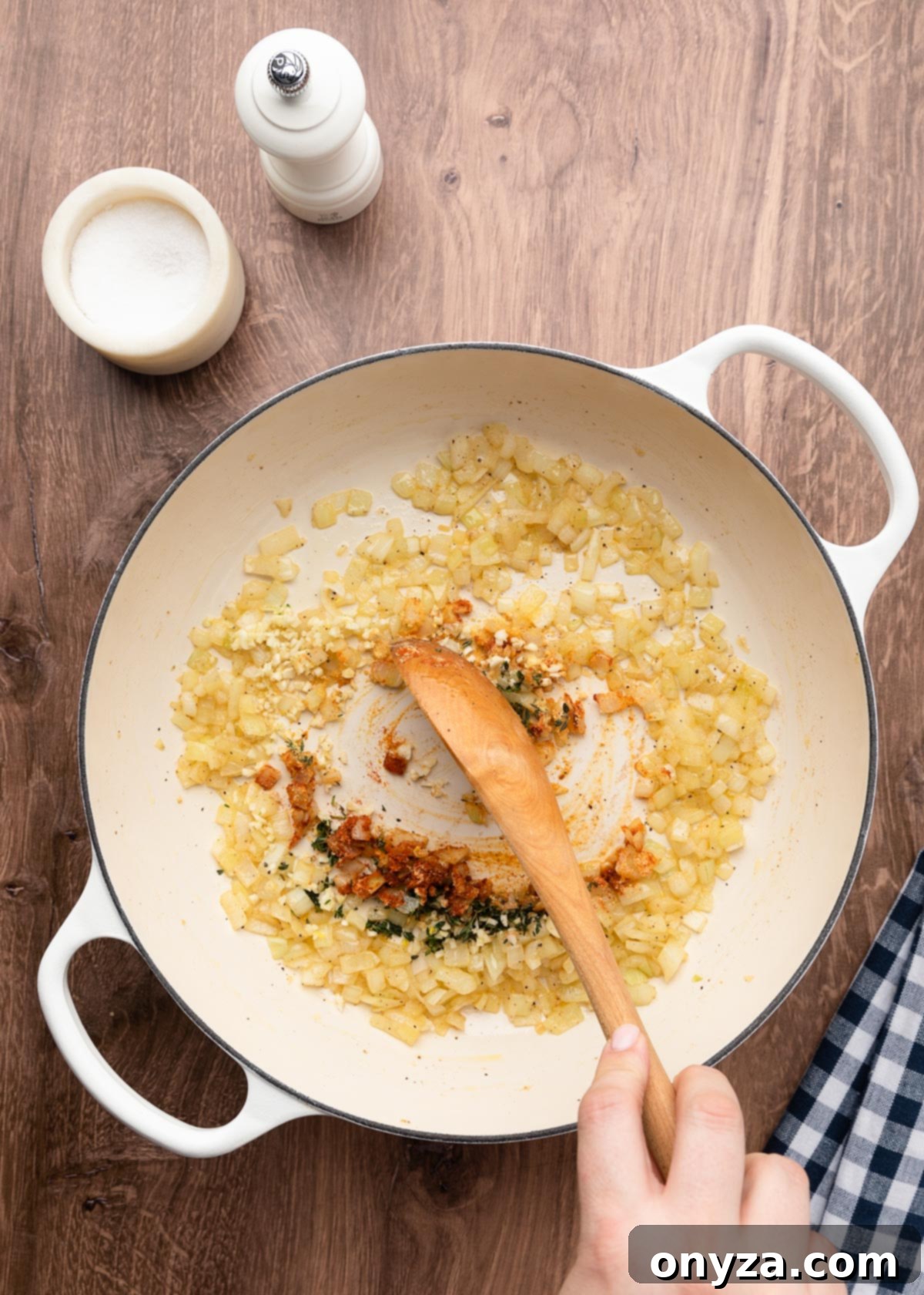Stirring minced garlic, fresh thyme, ground mustard powder, and sweet paprika into sautéed onions in a white enameled cast iron pot with a wooden spoon.