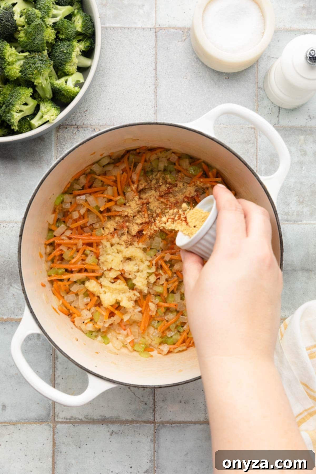 adding ground spices to sauteed carrots, onions, and celery in a white enameled cast iron dutch oven
