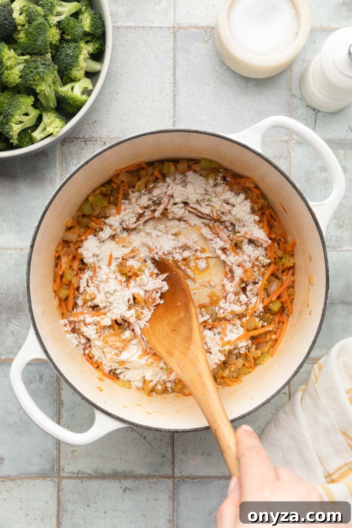 stirring flour into sauteed mirepoix in a white enameled cast iron dutch oven with a wooden spoon