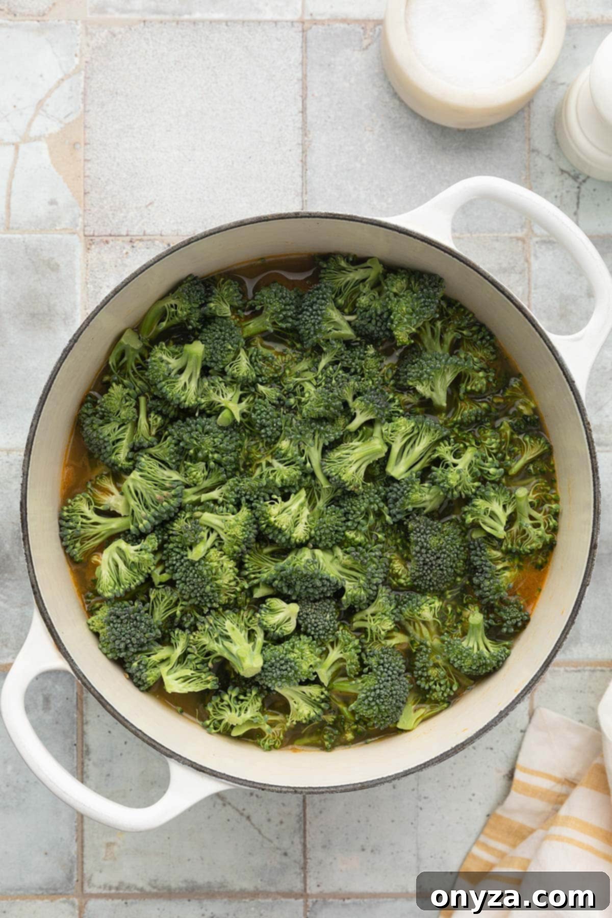 raw broccoli florets added to soup in a white enameled cast iron dutch oven