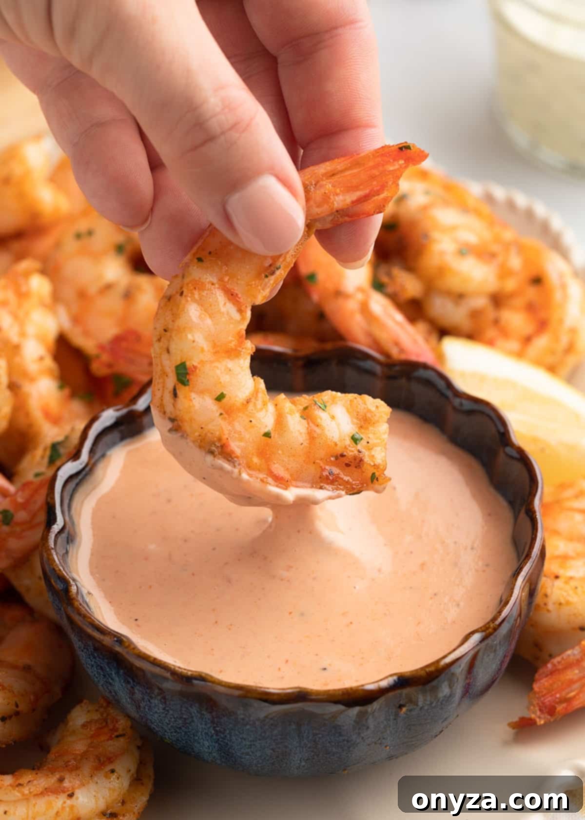 Crispy Air Fryer Shrimp 12 an air fried shrimp being dipped into a bowl of comeback sauce on a platter of shrimp with lemon wedges