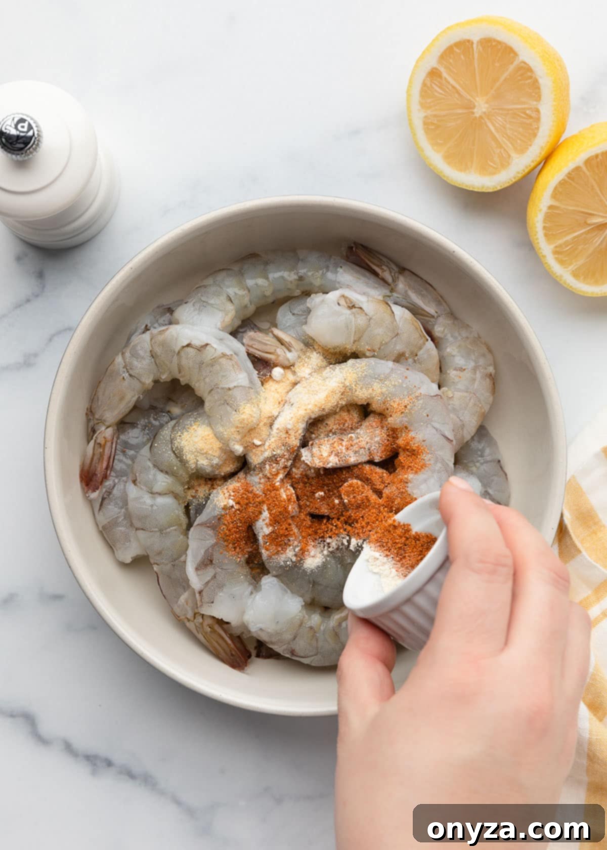 Crispy Air Fryer Shrimp 6 sprinkling ground spices over a bowl of raw shrimp from a tiny white ramekin