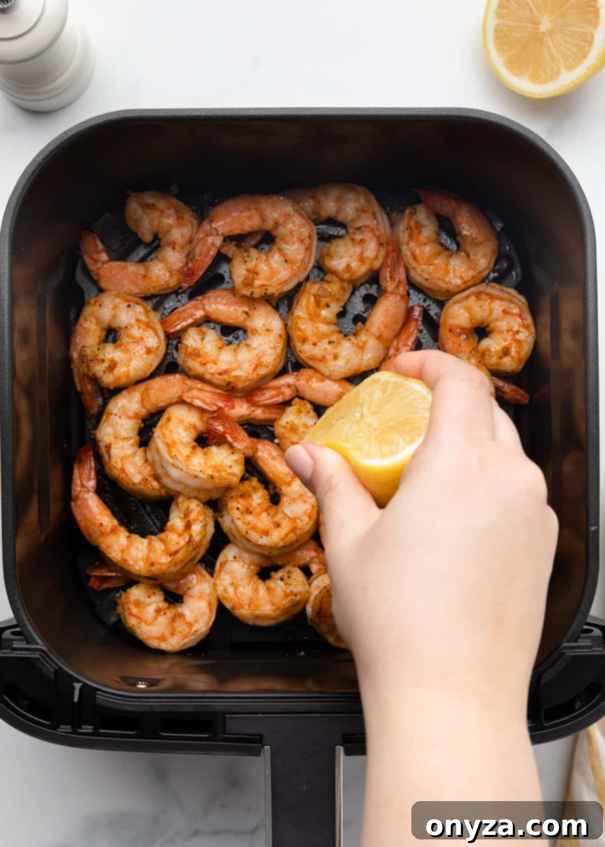 Crispy Air Fryer Shrimp 10 squeezing lemon juice from a halved lemon over cooked seasoned shrimp in a square XL air fryer basket
