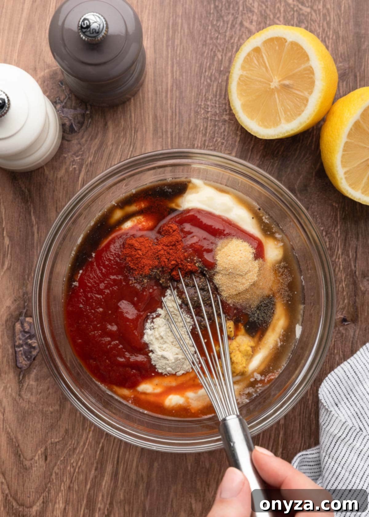A close-up shot of unmixed Comeback Sauce ingredients in a clear glass bowl, with a whisk resting beside it on a wooden board, ready for mixing.
