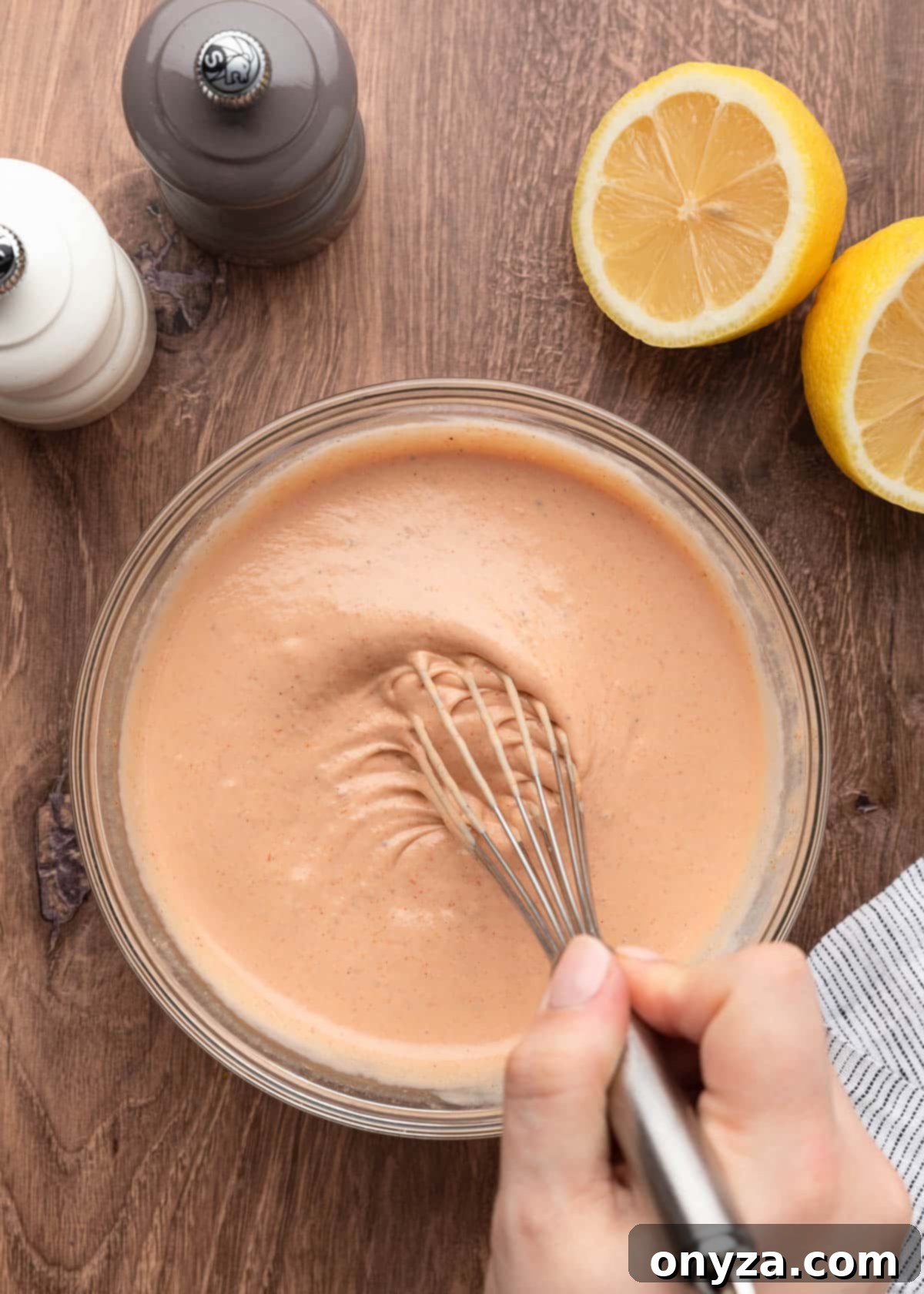 A glass bowl filled with fully mixed, creamy Comeback Sauce being stirred gently with a whisk on a wooden board, highlighting its smooth texture.