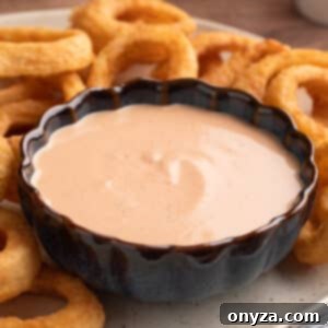 Comeback sauce in a blue scalloped bowl on a plate of onion rings, ready for serving.