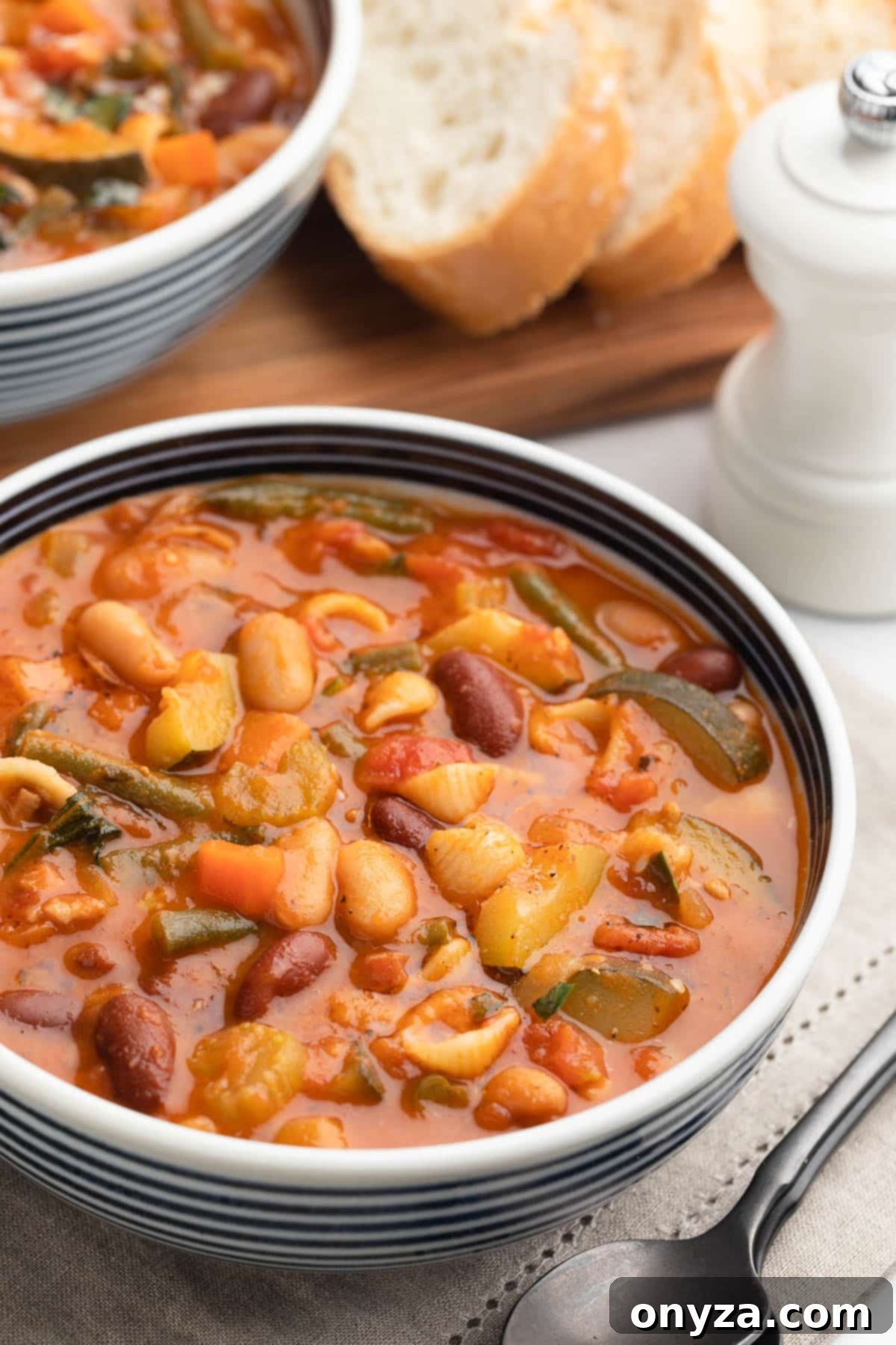 A beautifully presented bowl of Minestrone Soup with blue and white stripes, resting on a taupe napkin.