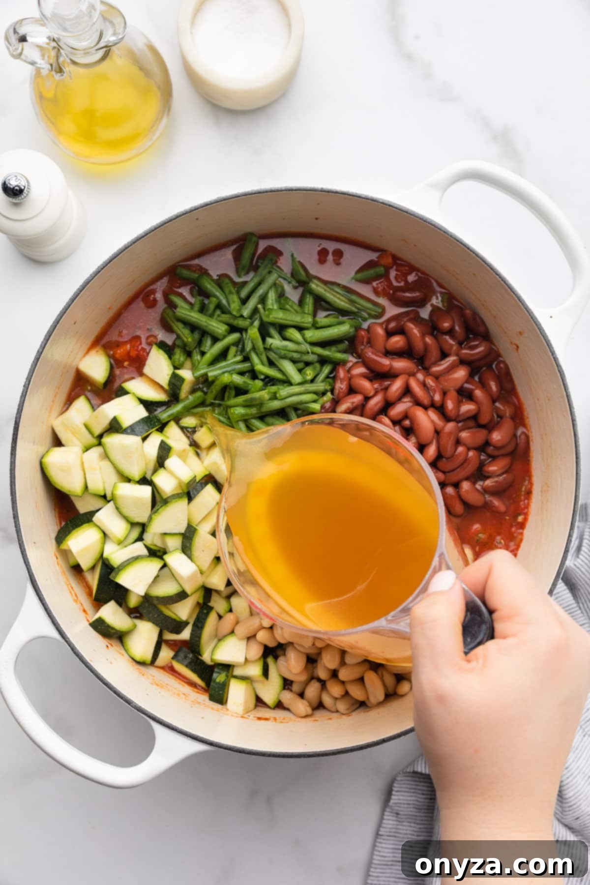 Pouring chicken stock from a liquid measuring cup into a pot of uncooked Minestrone Soup.