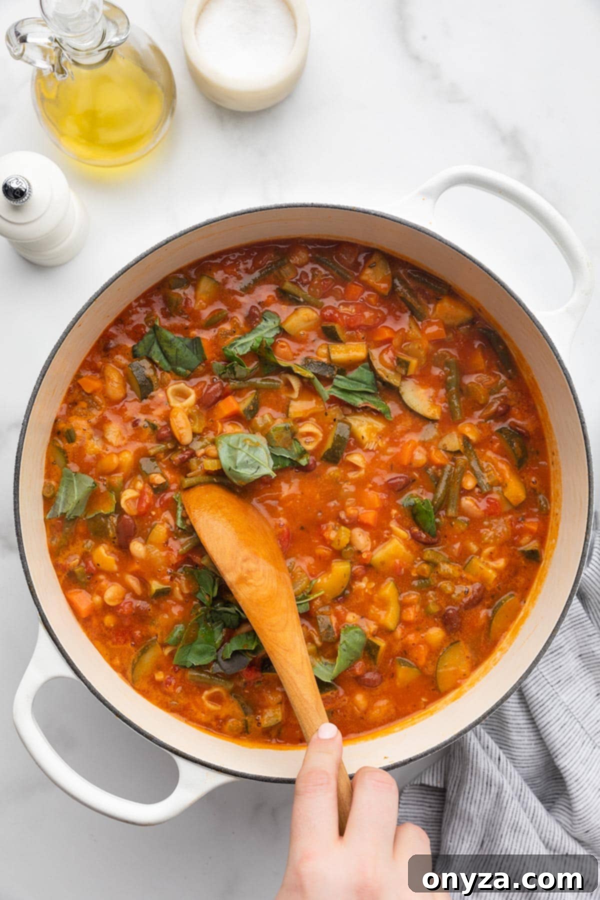 Stirring freshly torn basil leaves into a pot of Minestrone Soup with a wooden spoon, just before serving.