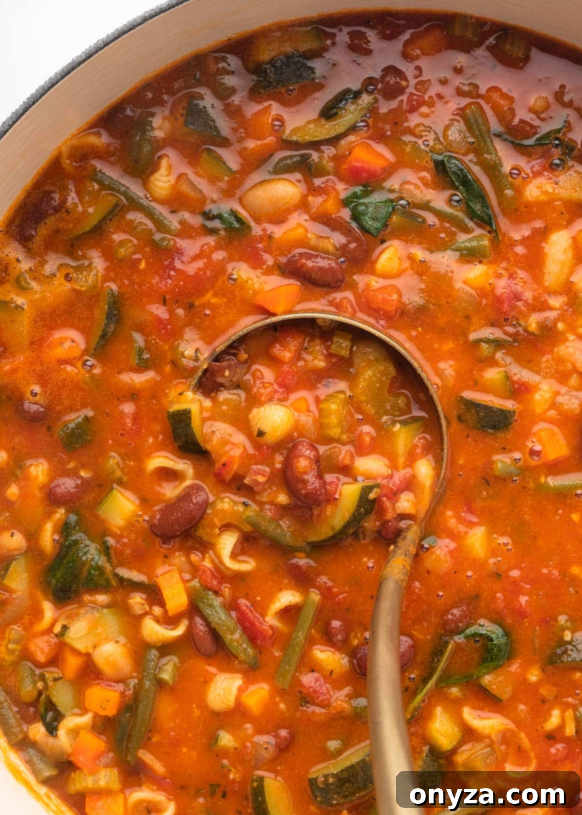 A close-up overhead shot of Minestrone Soup being ladled from a large pot, showing its rich texture and colorful ingredients.