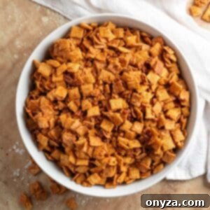 A stunning close-up of the cinnamon praline crunch snack mix, showcasing its golden, caramelized coating on crisp cereal and pecans, with a rich, inviting texture that promises irresistible flavor.