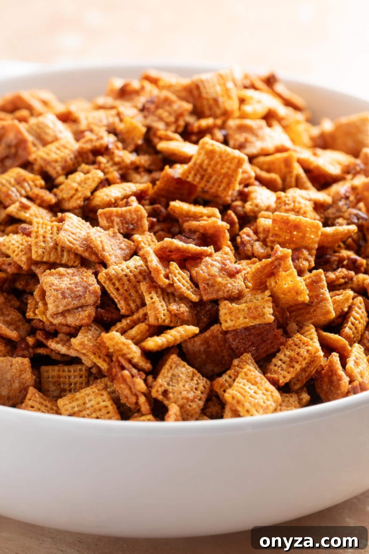 A mesmerizing close-up of a pristine white bowl overflowing with the delectable caramelized snack mix, where each crisp cereal square and succulent pecan is generously coated in a shimmering, golden praline glaze, highlighting its irresistible texture and sweet appeal.