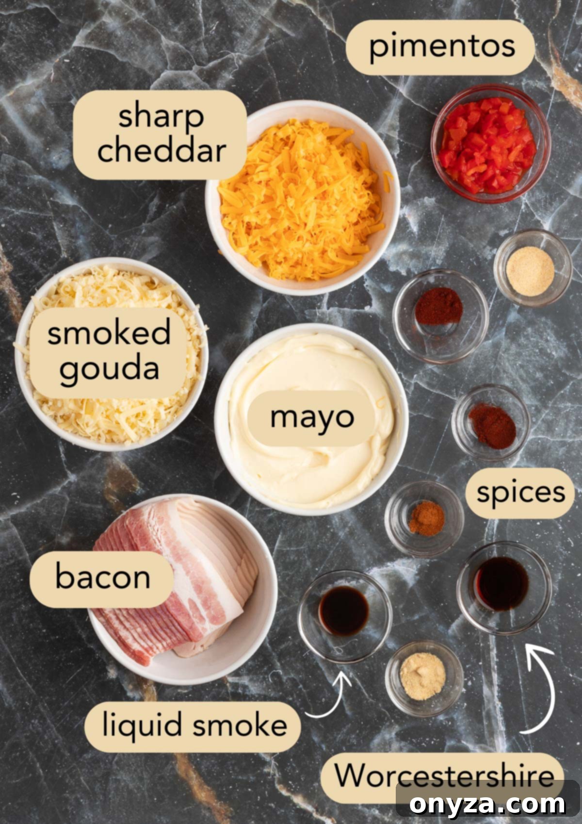 Overhead view of all ingredients required for smoky bacon pimento cheese, neatly arranged in bowls on a black marble surface.
