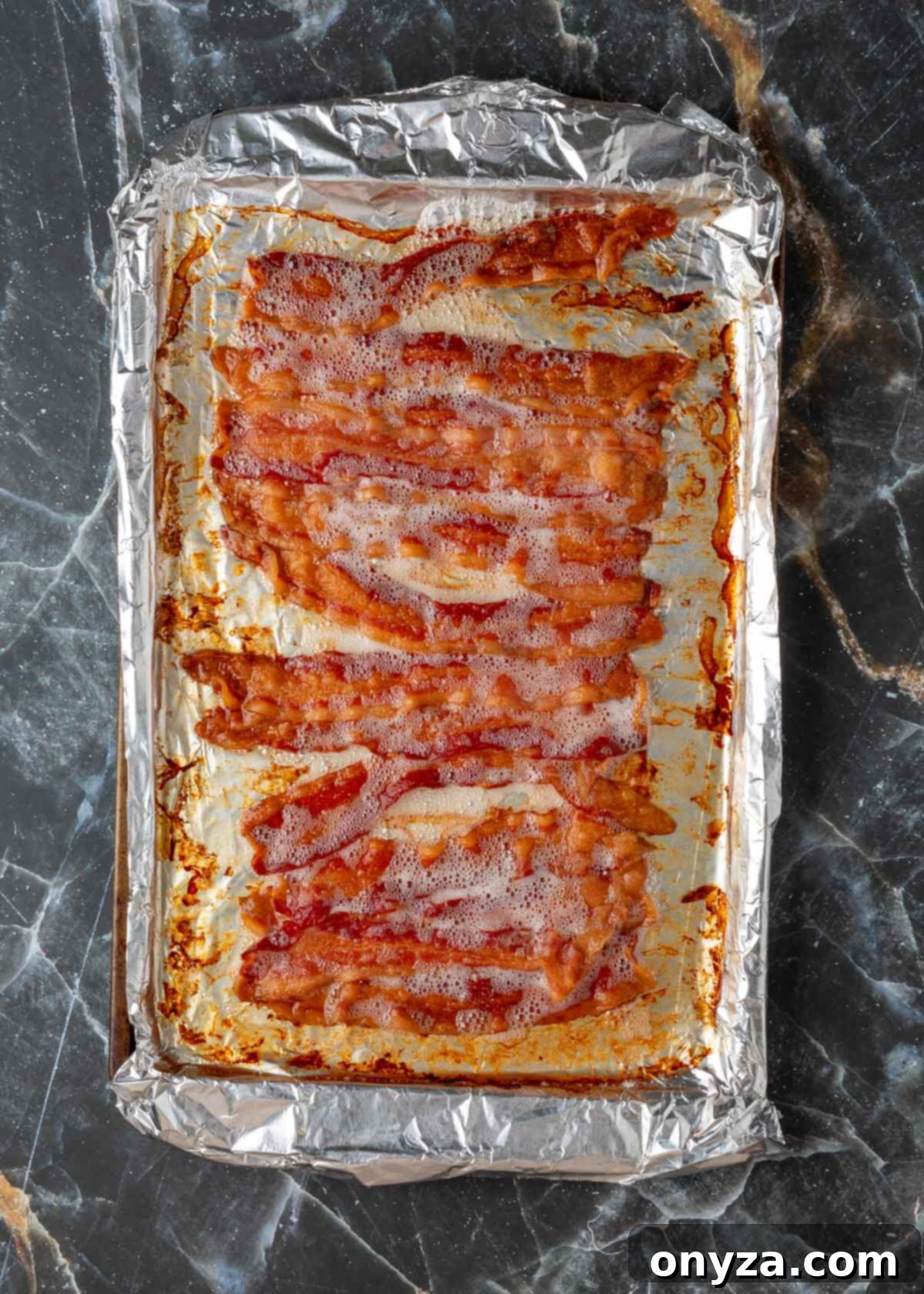 Crisp-cooked bacon, golden brown and perfectly rendered, resting on a foil-lined baking sheet after baking.