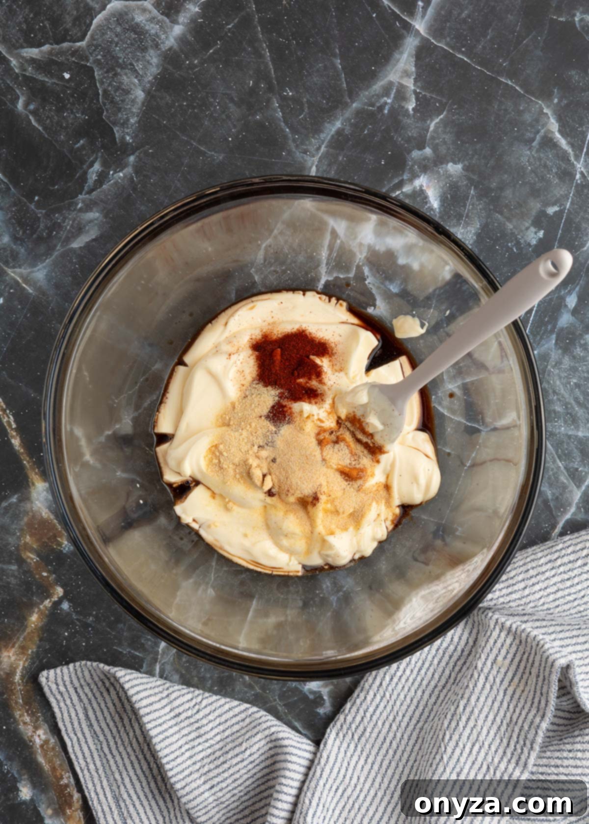 Mayonnaise, Worcestershire sauce, liquid smoke, and ground spices measured in small bowls on a black marble board, ready to be mixed.