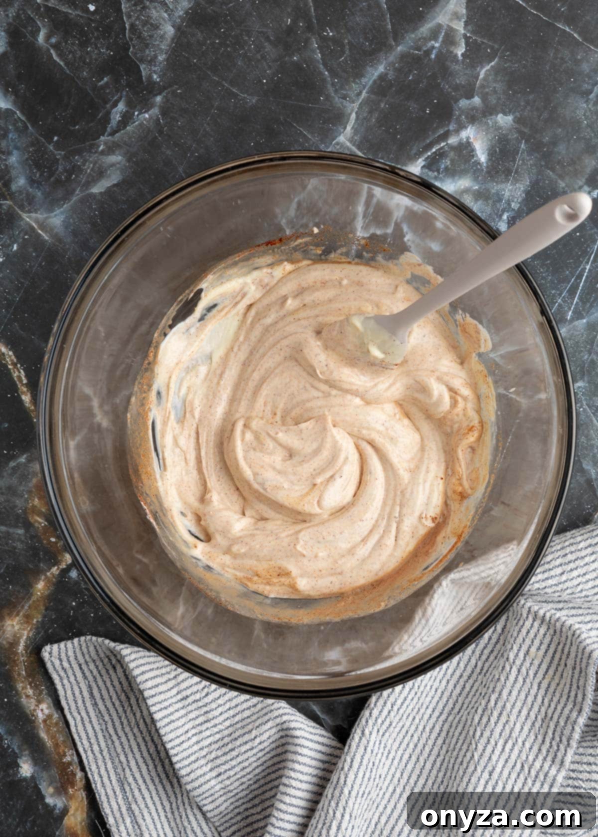 The mayonnaise base, seasoned with spices and liquid smoke, smoothly blended in a glass bowl with a rubber spatula.