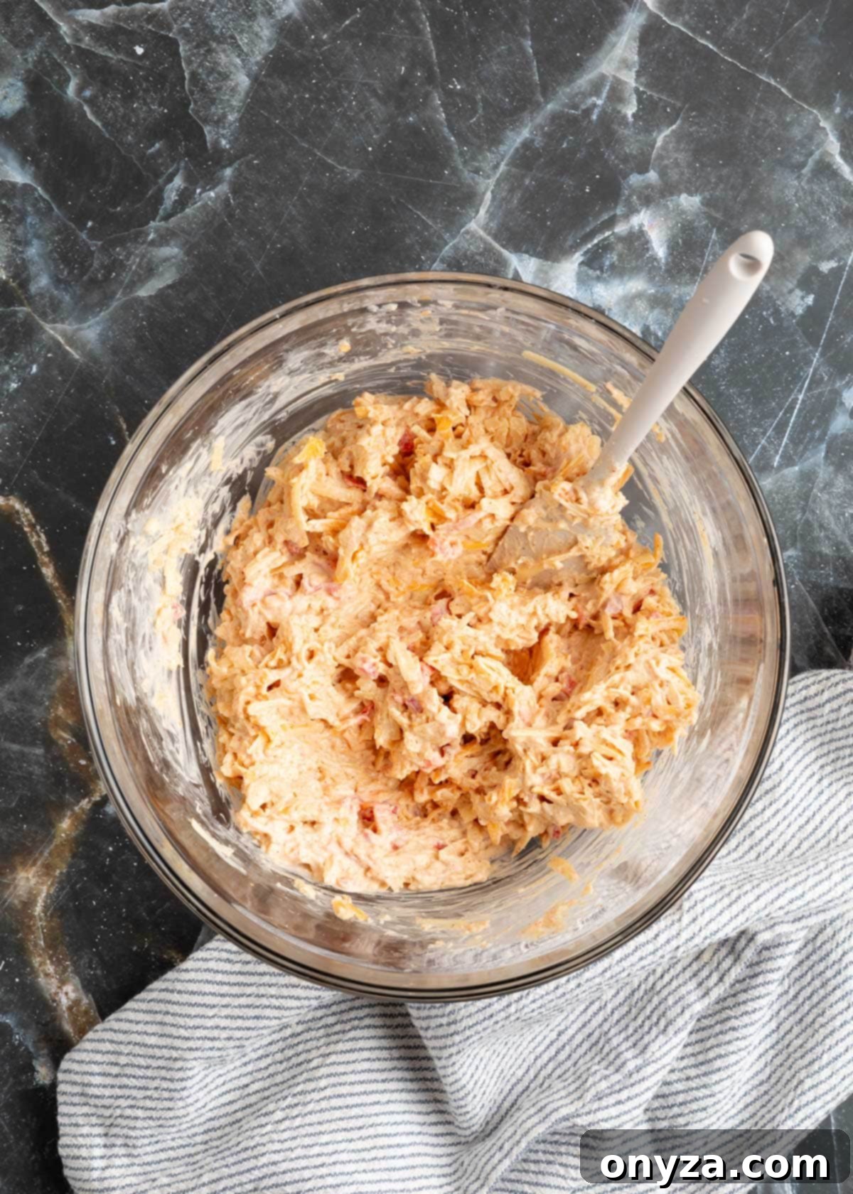 The fully mixed smoky bacon pimento cheese spread in a glass bowl, showcasing its rich texture and color.