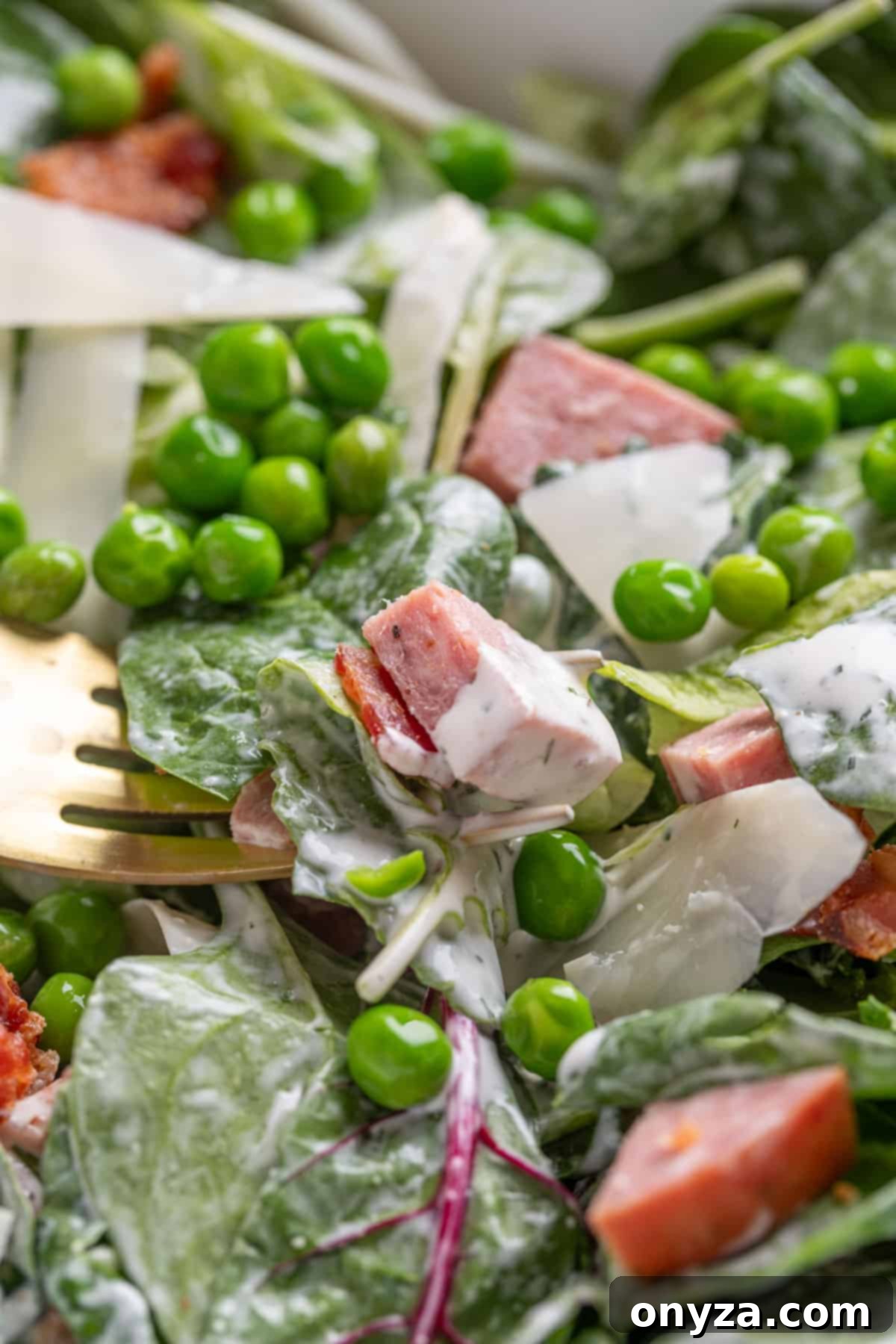 Savory Spinach & Pea Salad with Crispy Bacon and Sausage 11 Closeup of spinach and pea salad dressed with ranch dressing in a white bowl with a fork, ready to eat.