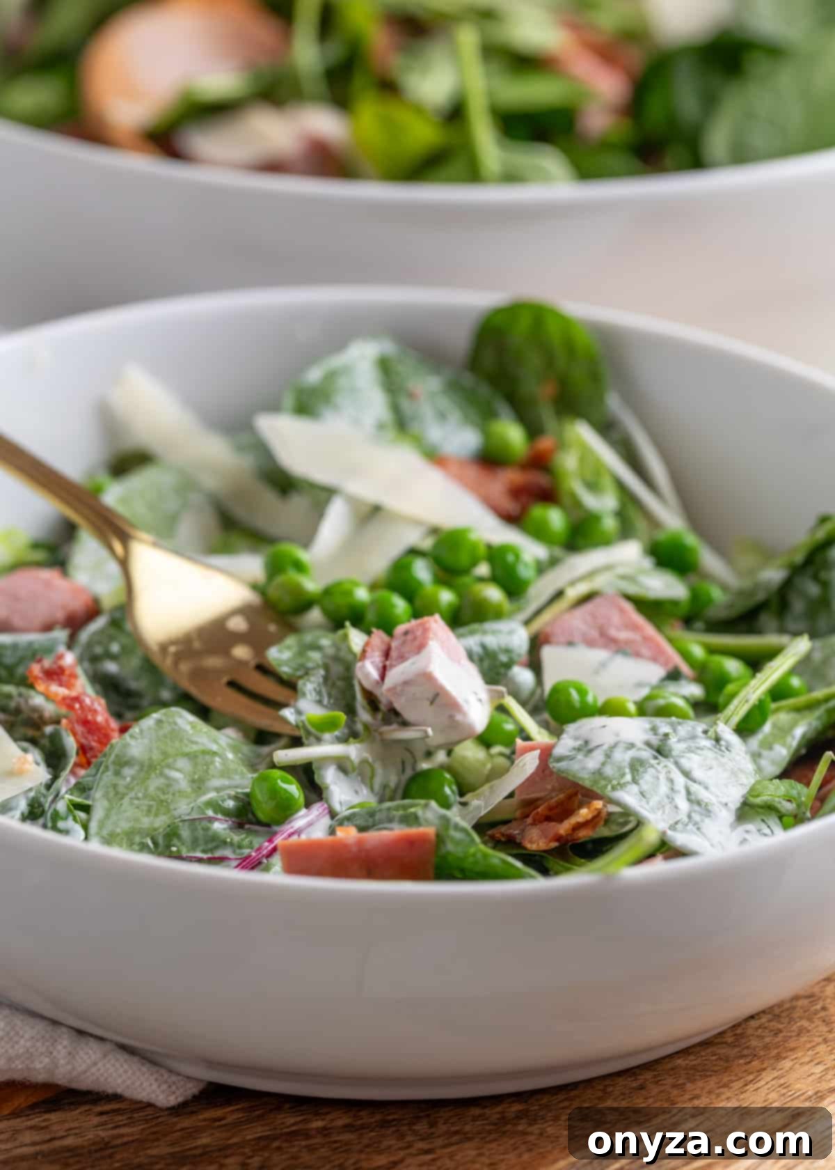 Savory Spinach & Pea Salad with Crispy Bacon and Sausage 12 Side view of spinach pea salad with dill ranch dressing in a white bowl with a gold fork, showing layers of ingredients.