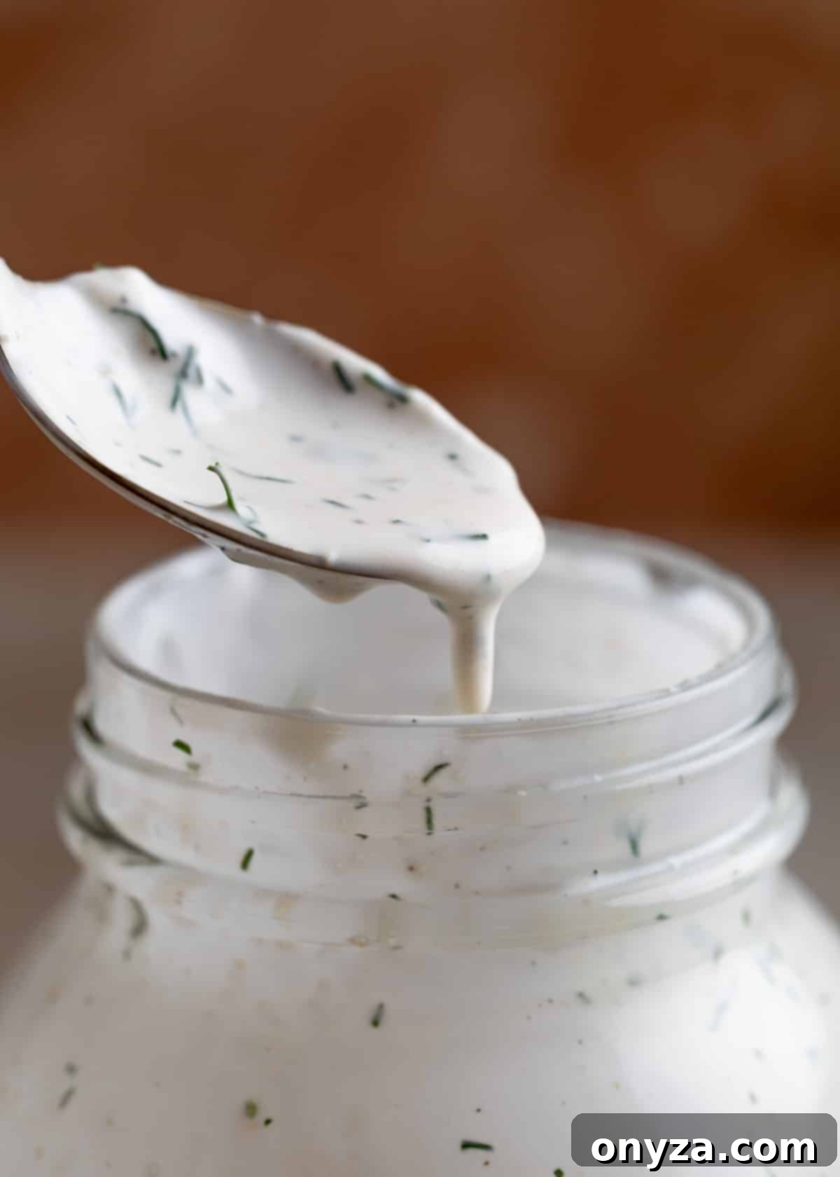 Savory Spinach & Pea Salad with Crispy Bacon and Sausage 6 Dill ranch dressing being drizzled from a spoon into a mason jar, showcasing its creamy texture.