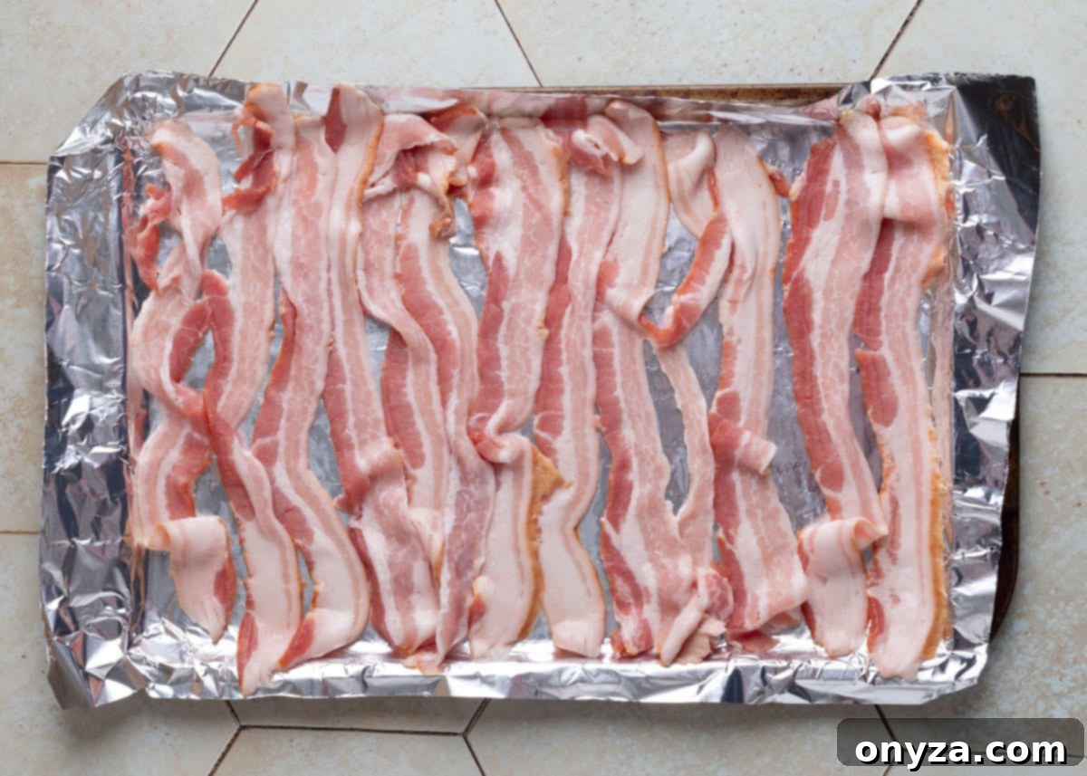 Savory Spinach & Pea Salad with Crispy Bacon and Sausage 7 Overhead view of raw bacon strips arranged on a foil-lined baking sheet, ready for the oven.