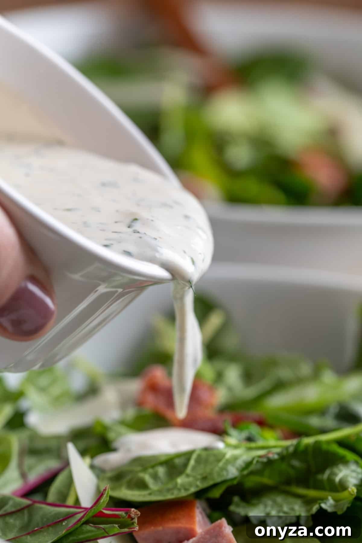 Savory Spinach & Pea Salad with Crispy Bacon and Sausage 10 Pouring dill ranch dressing over a spinach pea salad from a white cup, emphasizing the creamy texture.