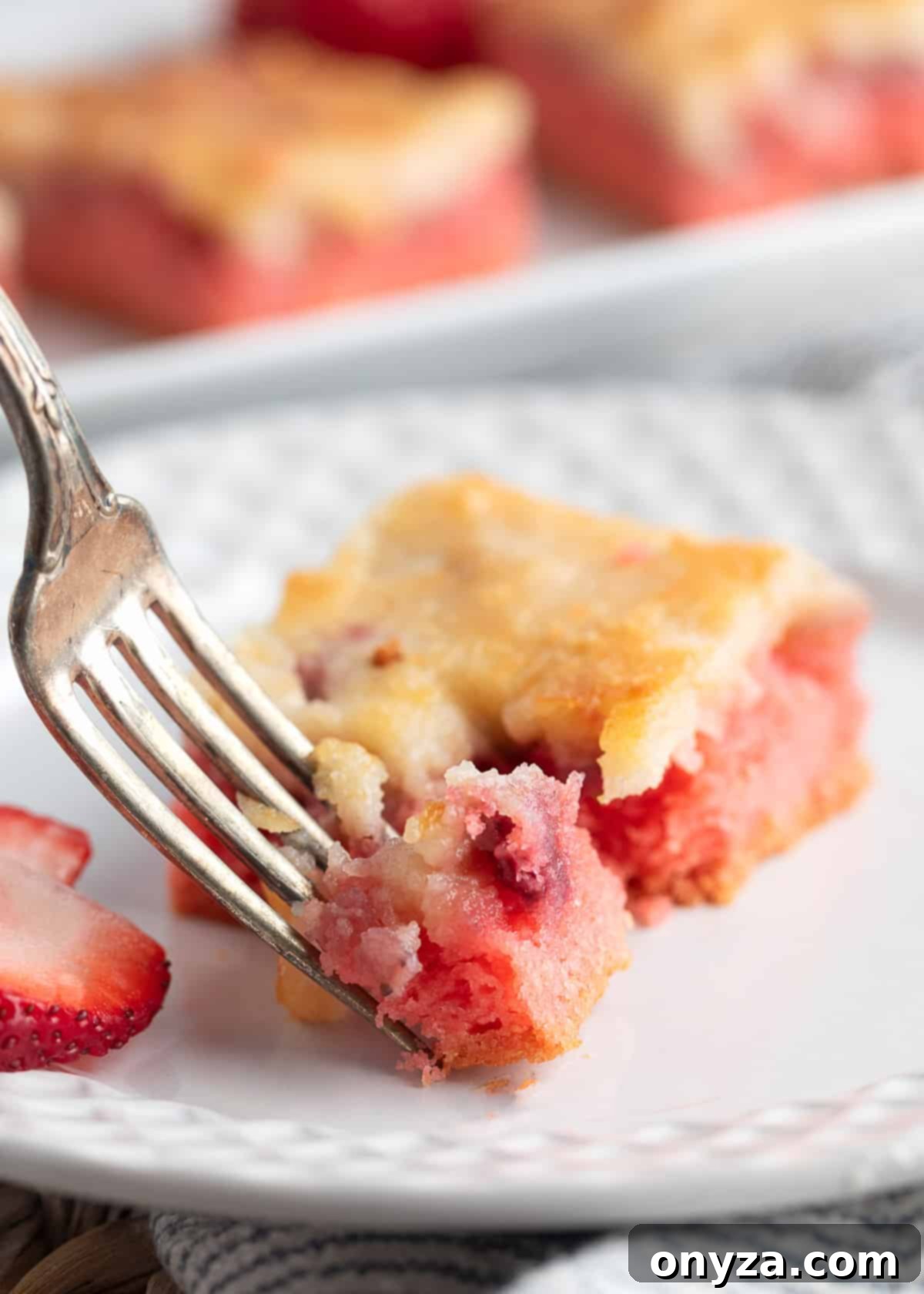 A perfectly baked strawberry chess square on a white plate being cut into with a silver fork, revealing its soft, gooey layers.