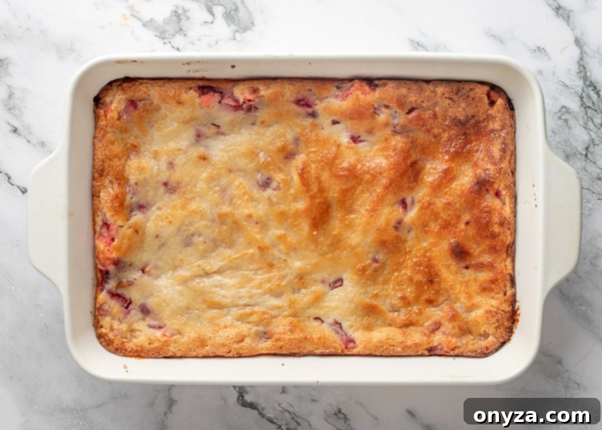 Overhead view of perfectly baked strawberry chess squares in a white baking dish on a white marble board, with a golden-brown topping.