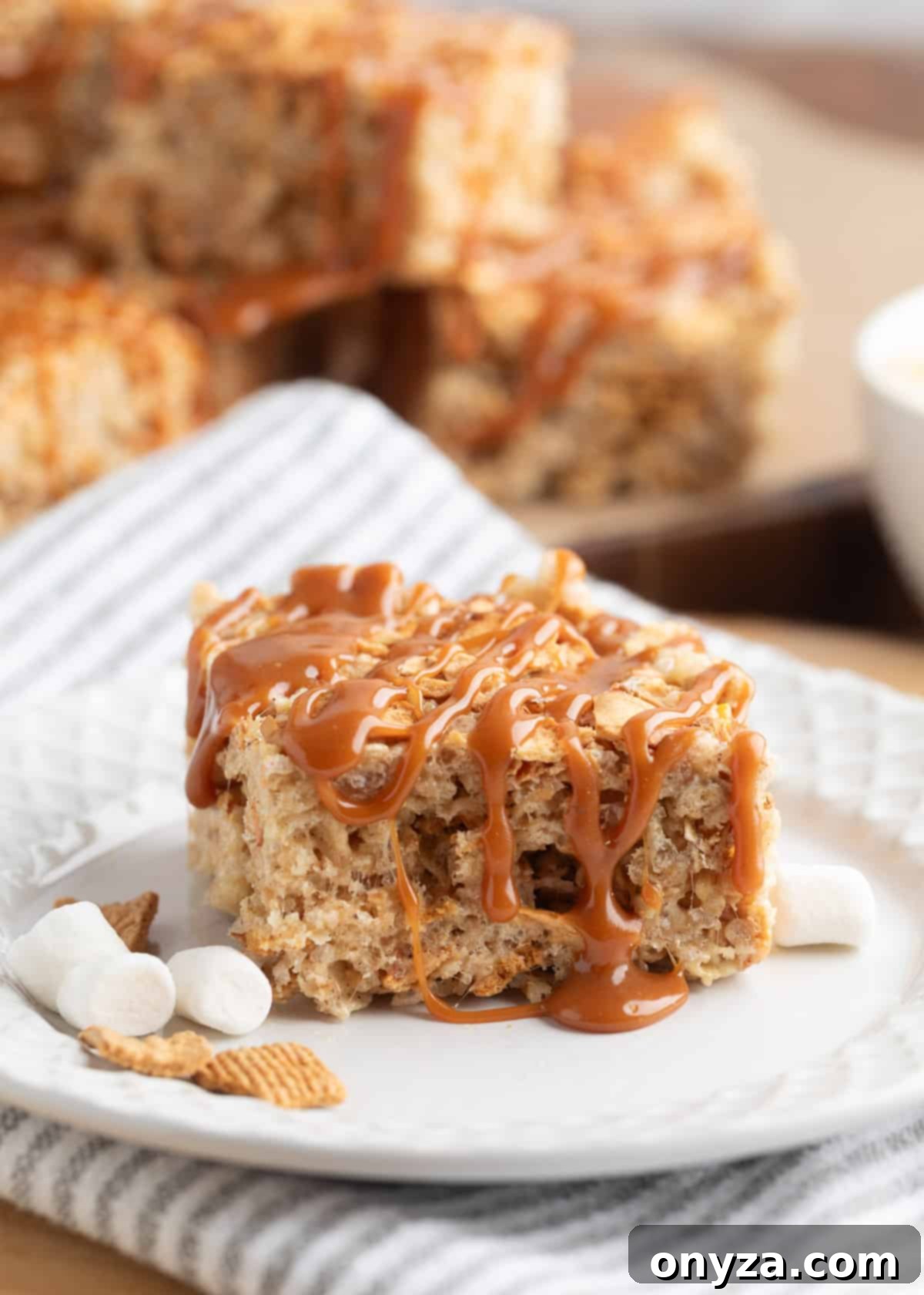 caramel apple pie rice krispie treat on a white plate next to marshmallows and golden grahams cereal