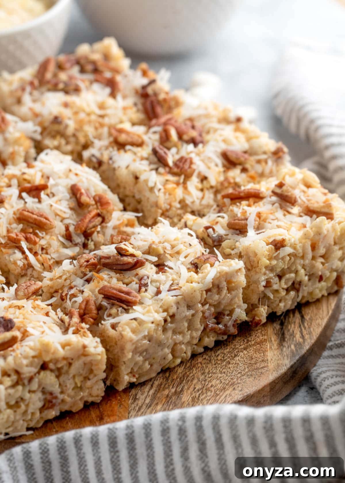 coconut pecan rice krispie treats cut into squares on a wood serving board with a gray and white striped napkin