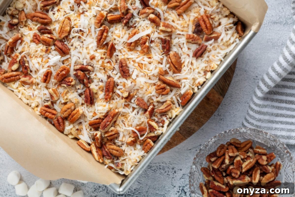 overhead of coconut pecan rice krispie treats in a parchment lined pan next to a bowl of pecans