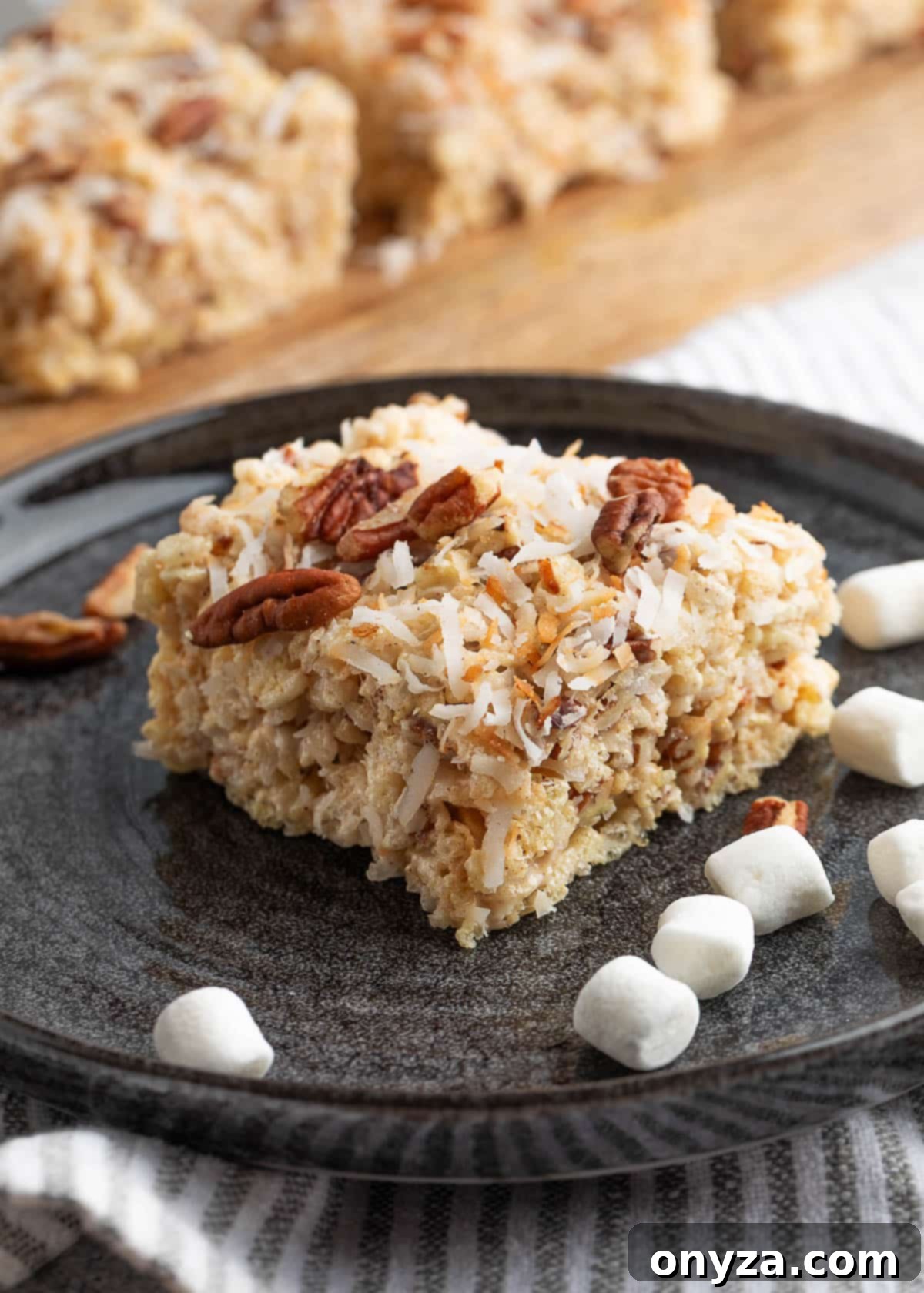 coconut pecan rice krispie treat served on a black plate scattered with mini marshmallows