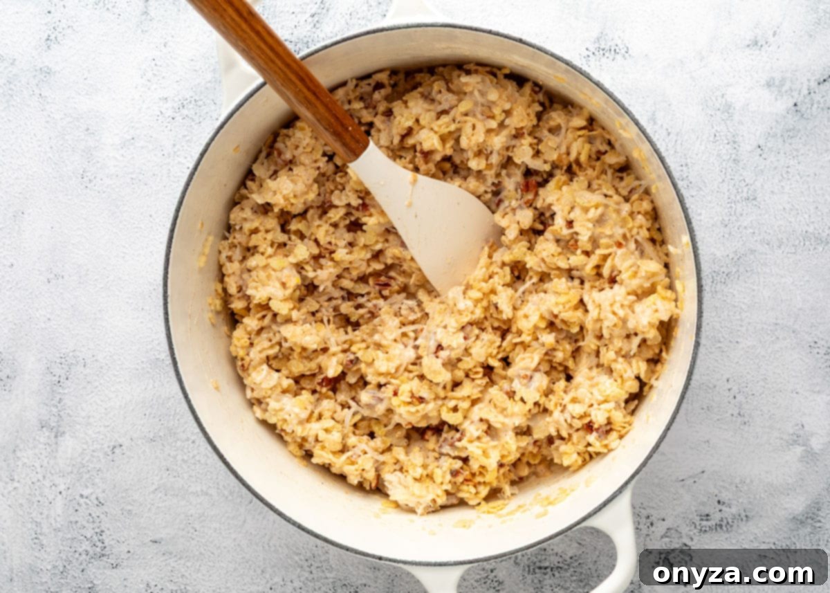 Mixed coconut pecan rice krispies treats in a white enameled cast iron pot with a wood handled spatula