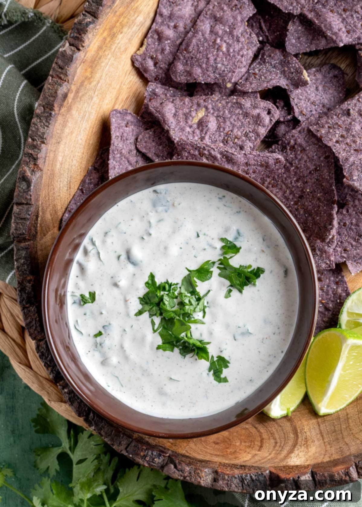 Southwestern Green Chile Cilantro Dip 2 overhead of green chile dip with cilantro in a brown bowl on a platter with blue corn tortilla chips and lime wedges