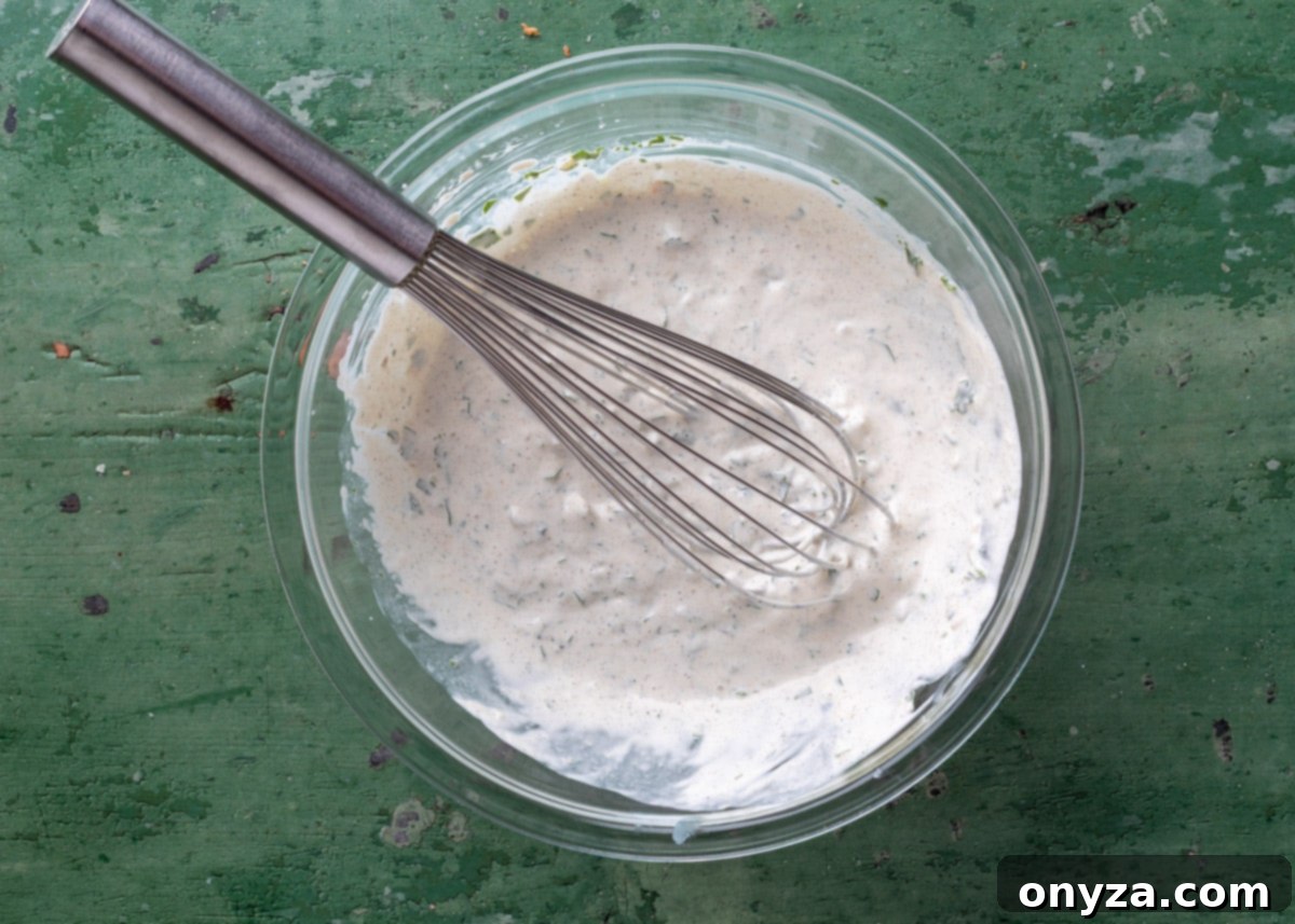 Southwestern Green Chile Cilantro Dip 5 green chile cilantro dip mixed in a glass bowl with a stainless steel whisk on a green board