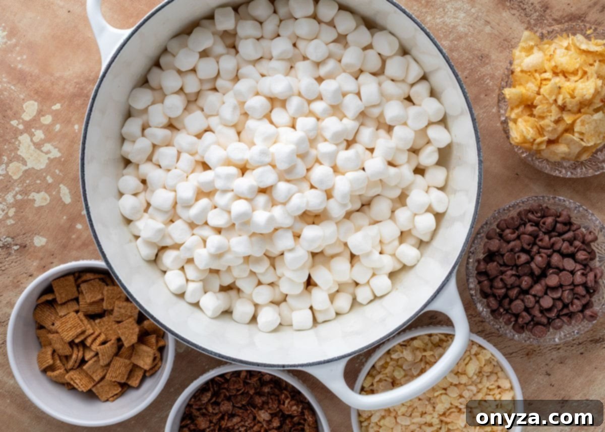 A large white Dutch oven filled with mini marshmallows, about to be melted for rice krispie treats. Various mix-in ingredients including crushed chips, chocolate chips, and assorted cereals are arranged around the pot.