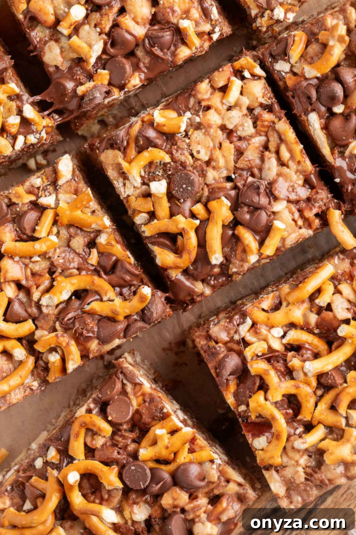 Close-up overhead view of sliced loaded rice krispie treats on parchment. The bars are packed with pretzel twists, chocolate chips, chopped nuts, and cereal, with gooey melted chocolate visible between pieces. 