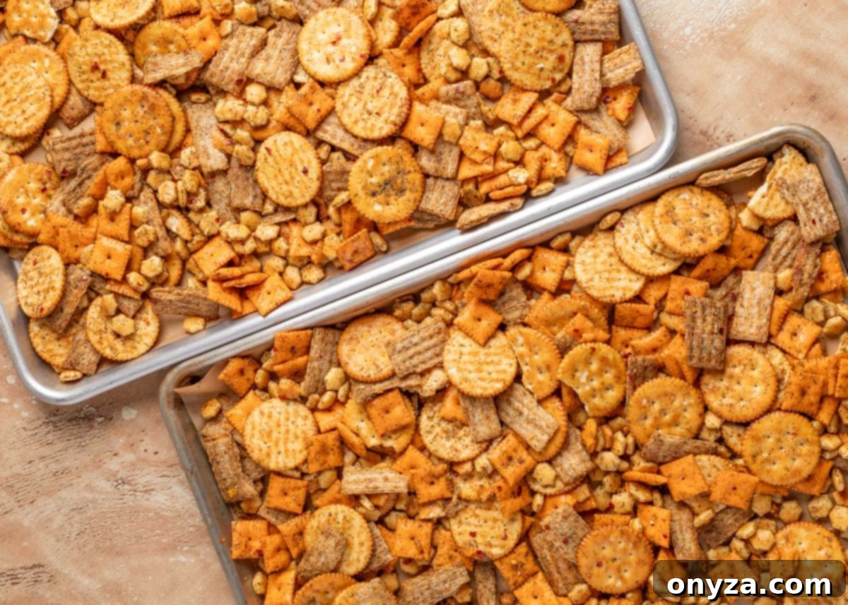 Zesty Dill Ranch Crackers 5 Two baking sheets filled with seasoned dill ranch snack mix, including cheese crackers, wheat crackers, butter crackers, and oyster crackers, arranged on a tan surface.