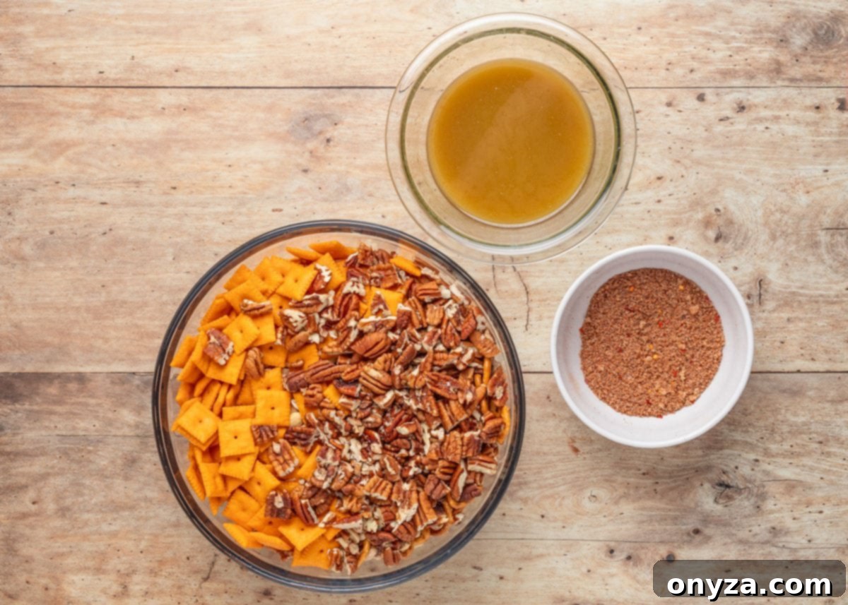 A top-down view of a glass mixing bowl filled with cheese crackers, chopped pecans, and pretzels on a wooden surface. To the upper right, there’s a small bowl of barbecue seasoning blend and a larger bowl with a melted butter mixture. The image illustrates the prep stage for making BBQ snack mix.