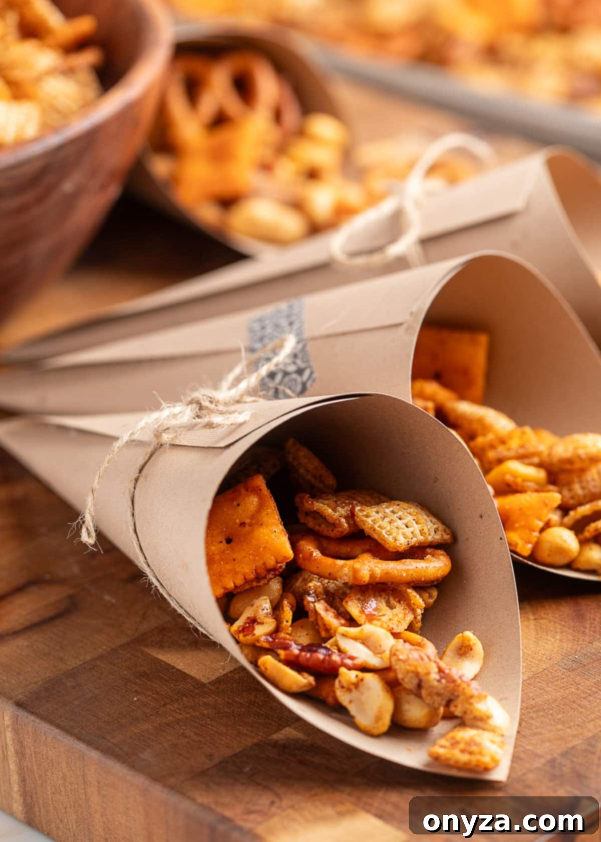 BBQ snack mix served in brown paper cones tied with twine, filled with Chex cereal, pretzels, peanuts, and cheesy crackers, arranged on a wooden board for individual snacking.