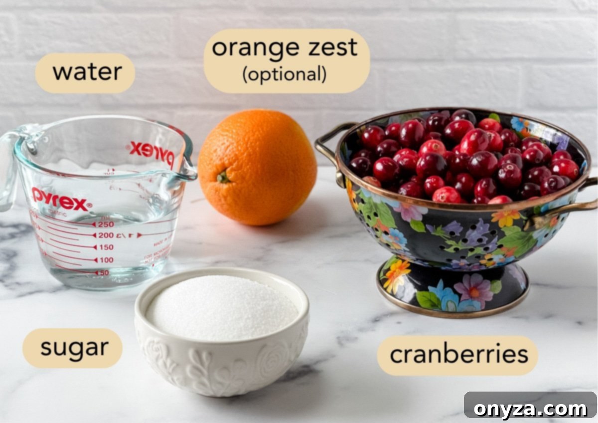 Overhead view of ingredients for homemade cranberry sauce, labeled with text: a glass measuring cup of water, a whole orange labeled “orange zest (optional),” a black floral colander filled with fresh cranberries, and a white bowl of sugar.