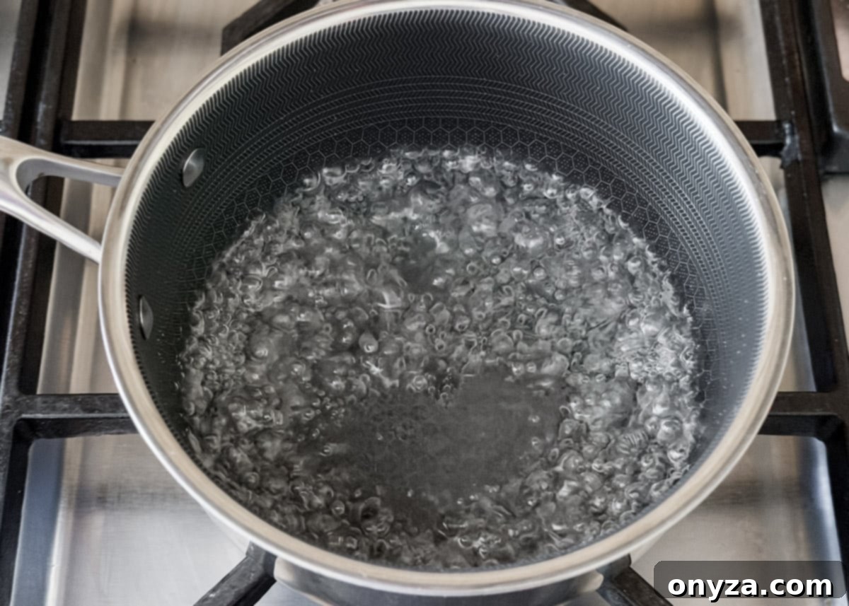 A close-up of a saucepan on a stovetop with sugar water at a rolling boil, ready for the next step in the recipe.