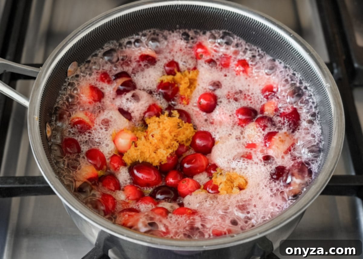 Cranberries and orange zest simmering in a saucepan as the mixture begins to boil and foam.