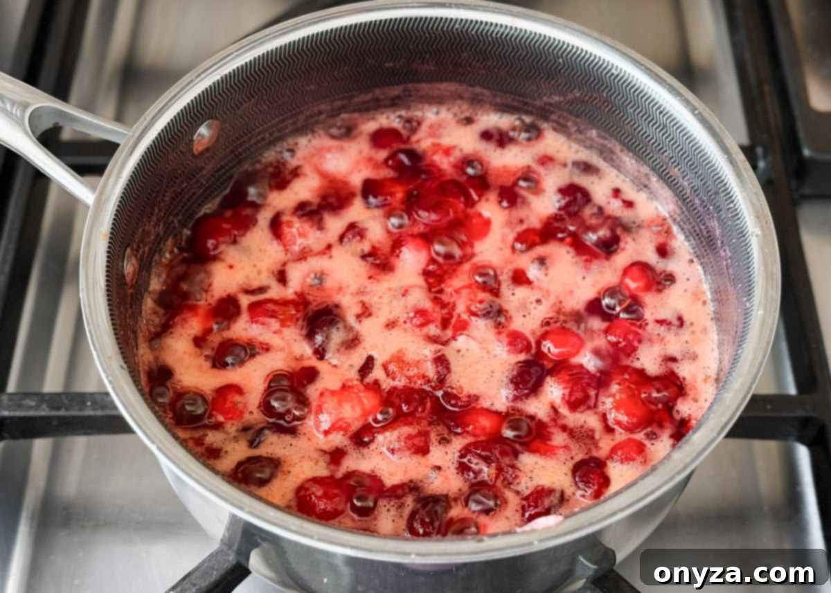 Cranberries cooking in a saucepan, starting to burst and release their juices into the bubbling mixture.
