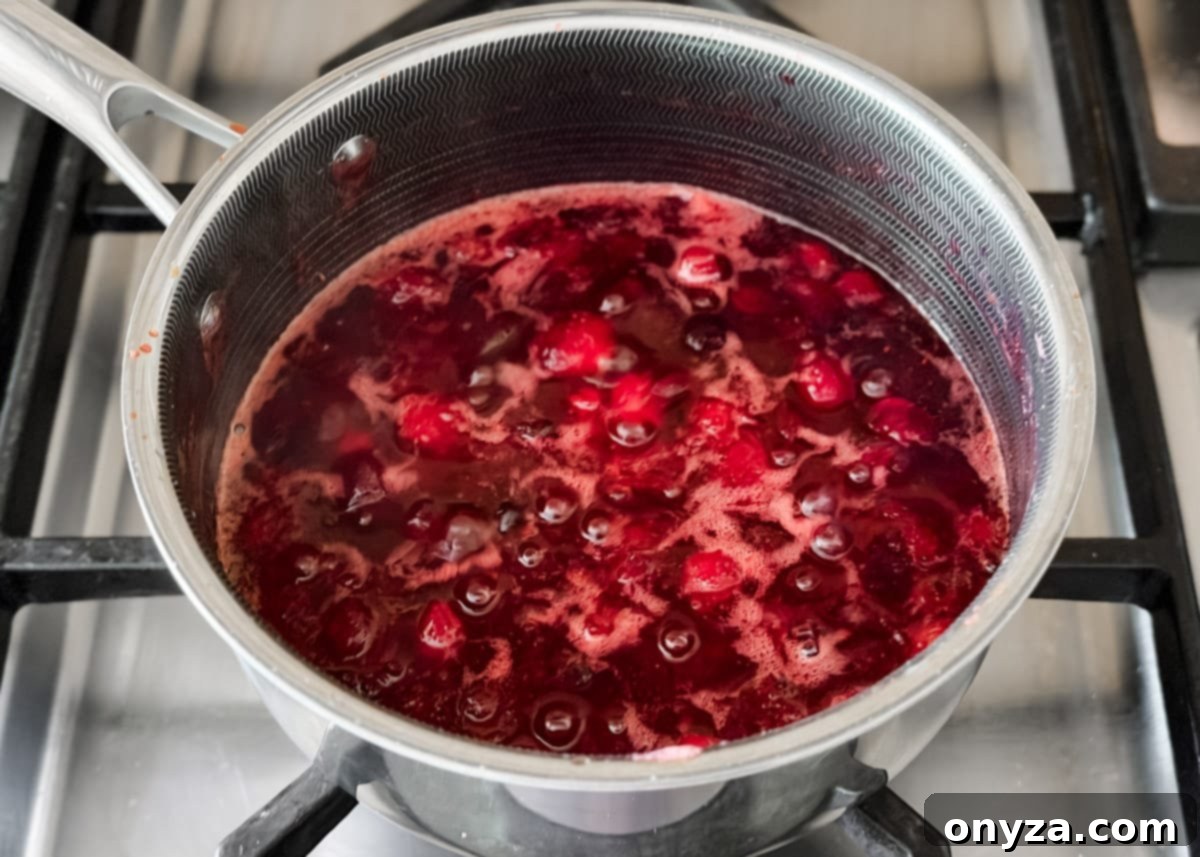 Cranberries simmering and breaking down in the saucepan as the sauce thickens and deepens in color.