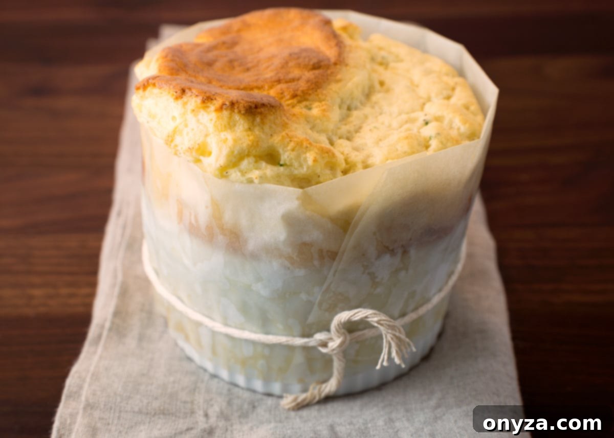 A perfectly baked cauliflower soufflé, still in its white ramekin with the parchment collar attached, resting on a beige linen napkin, ready for serving.