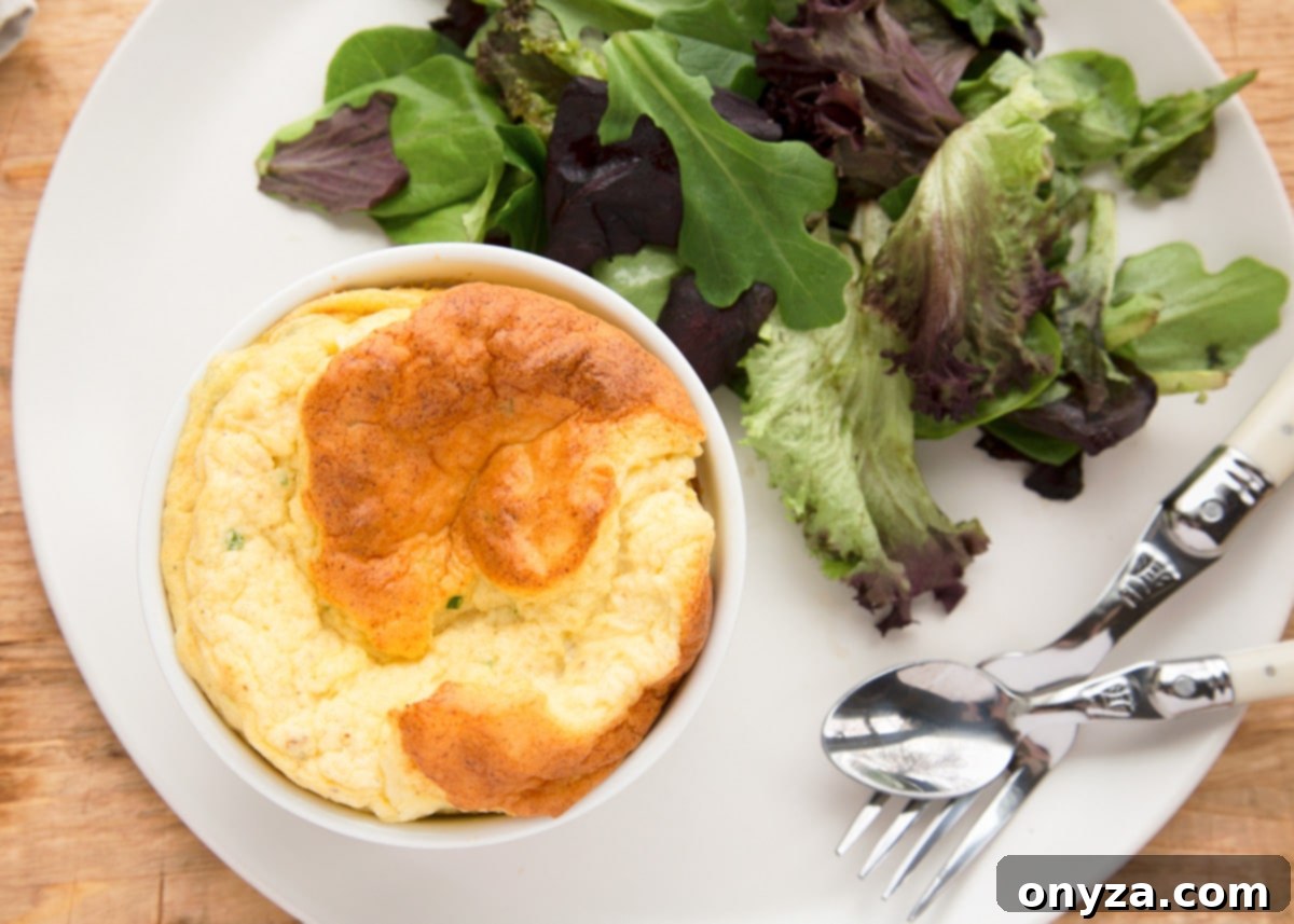 A perfectly baked cauliflower soufflé on a white plate, accompanied by a fresh green salad, with a fork and spoon nearby.